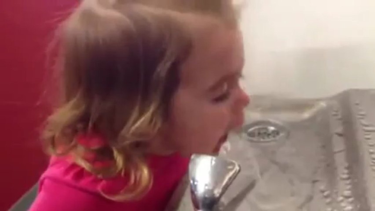 Cette petite fille essaye tant bien que mal de boire à la fontaine à eau