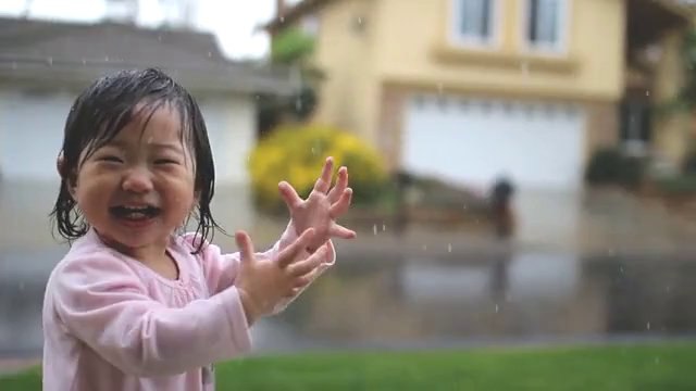 Une petite fille découvre la pluie et joue sous les gouttes... Trop mignon!