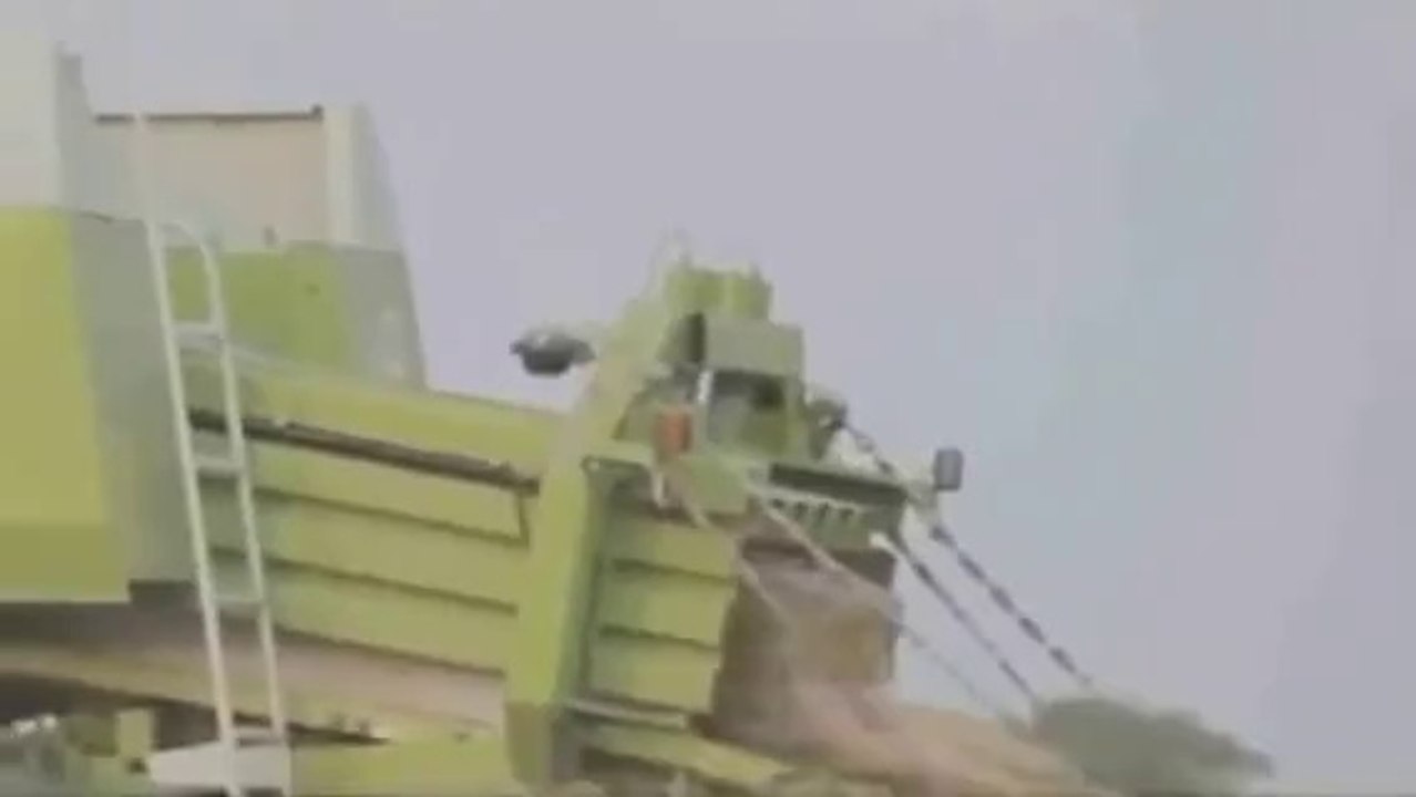 Un homme passe dans une machine à faire des ballots de paille