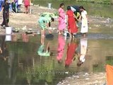 Assamese women wash utensils in a dirty pond, Assam