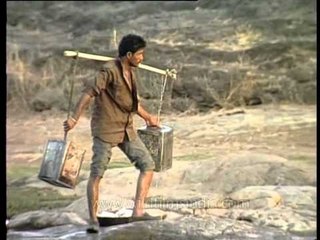 Maldhari man carrying water-filled tin containers using a suspended pole