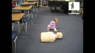 Baby girl practices CPR on a dummy...