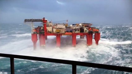 Huge waves crash against swaying North Sea oil rig