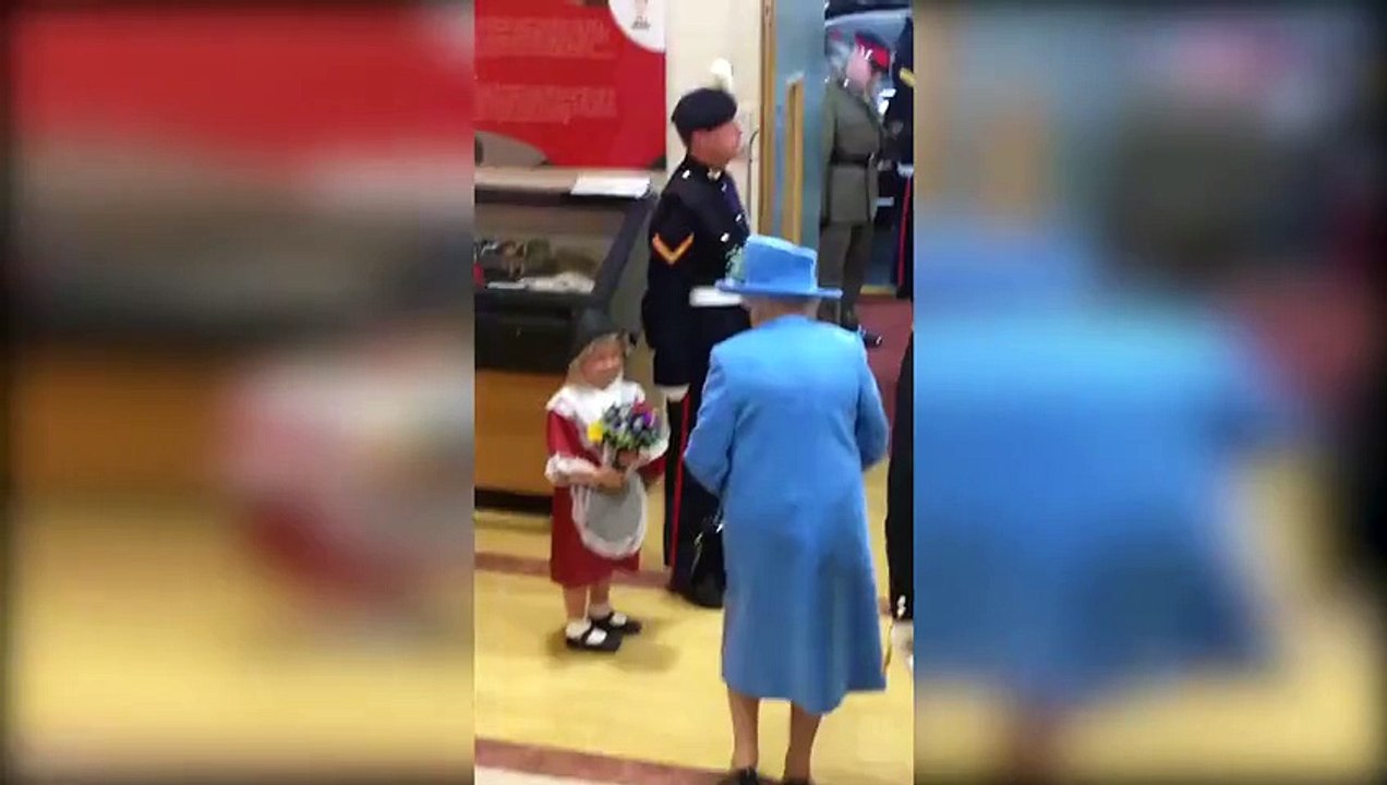 Ouch! Little girl presents a posy to the Queen... only to be smacked on the head by a saluting soldier