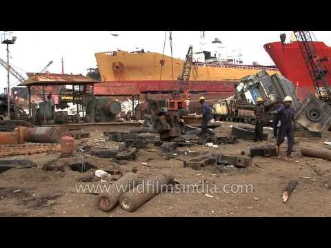 Labourers lift heavy metal structures on crane at a ship breaking yard in Alang