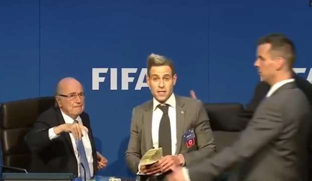 Lee Nelson balance des billets sur Sepp Blatter lors d'une conférence de presse