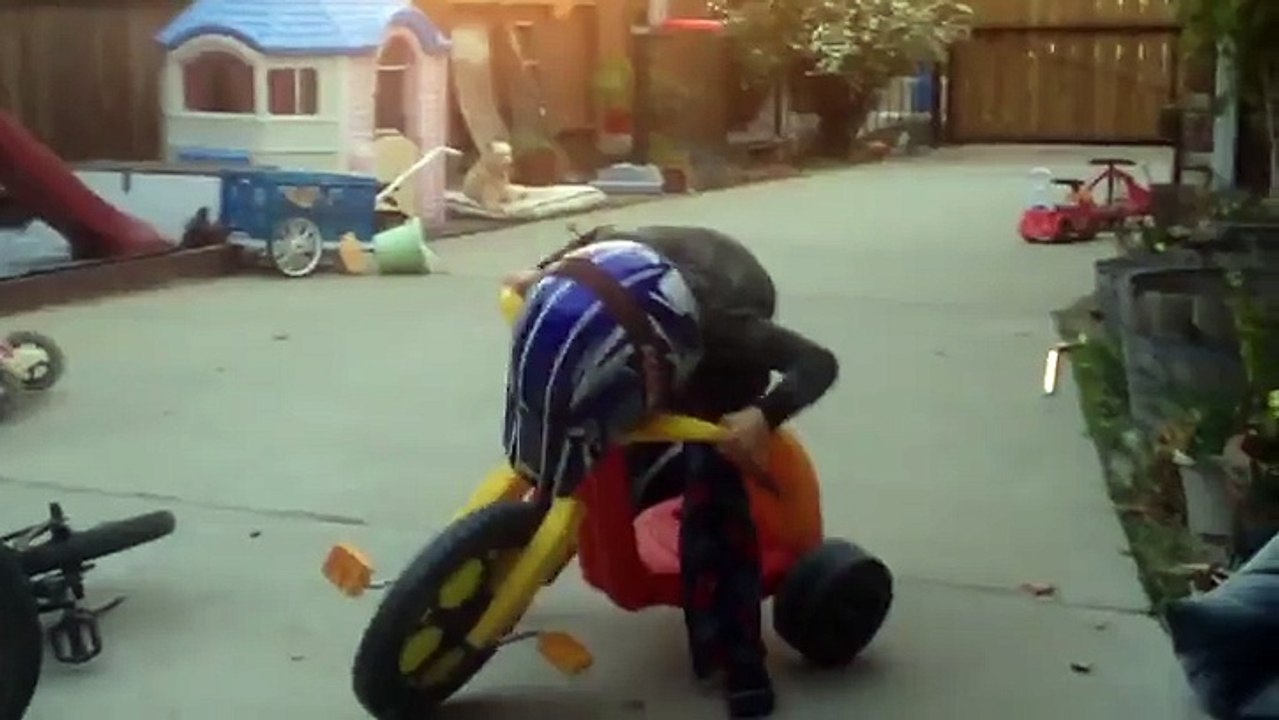 Il se coince la tête avec son casque et son tricycle
