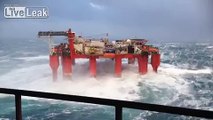 Huge waves crash against swaying North Sea oil rig