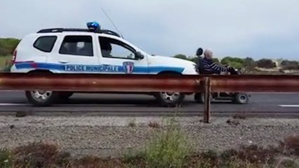 Un vieil homme en fauteuil roulant se fait pousser par une voiture de police