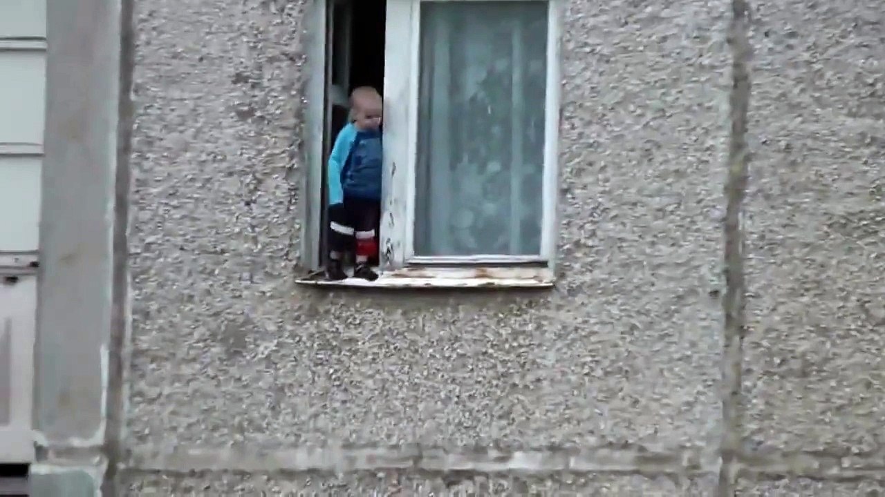 Un enfant joue sur le bord d'une fenêtre au 8ème étage