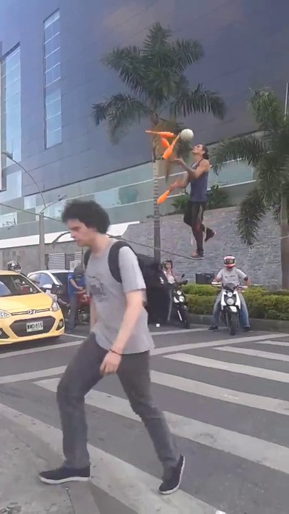 Guy does tight rope juggling tricks on street while traffic lights are red