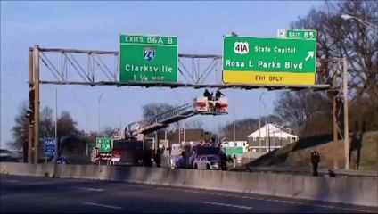 Un homme se suspend aux panneaux de signalisation au dessus d'une autoroute