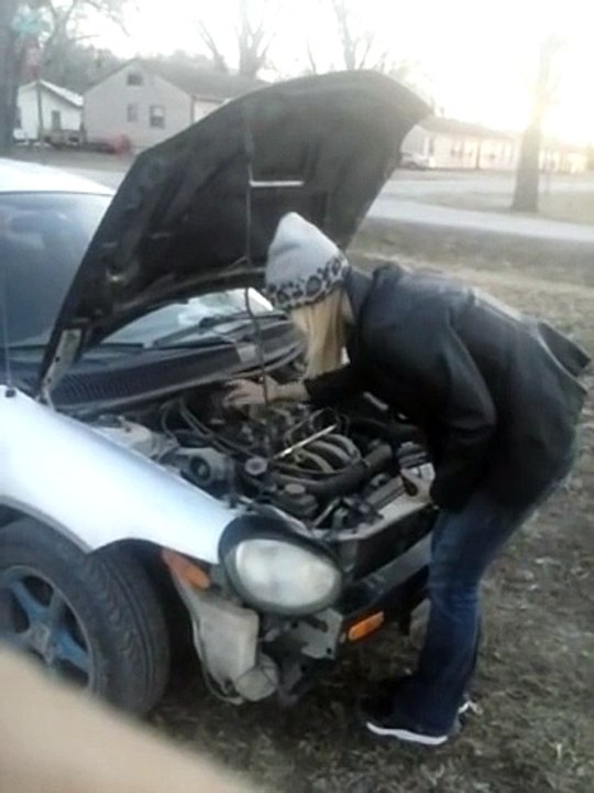 Une blonde met de l'huile dans sa voiture