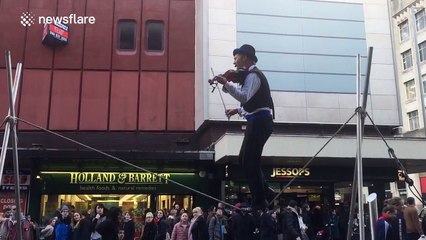 Man plays violin while tightrope walking in Manchester