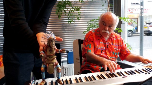 Une marionnette danse avec un pianiste qui joue dans un restaurant...
