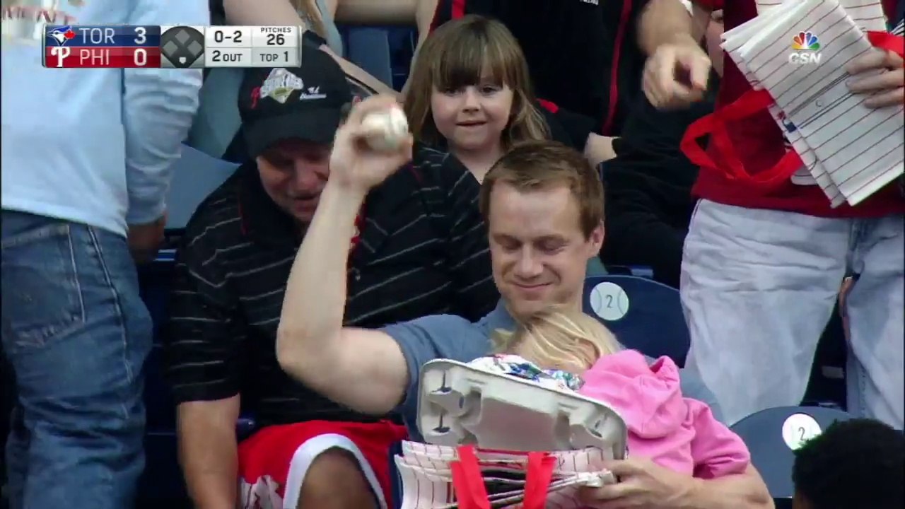 Papa attrape une balle de Baseball avec un bébé dans les mains en plein match dans les tribunes