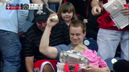 Papa attrape une balle de Baseball avec un bébé dans les mains en plein match dans les tribunes