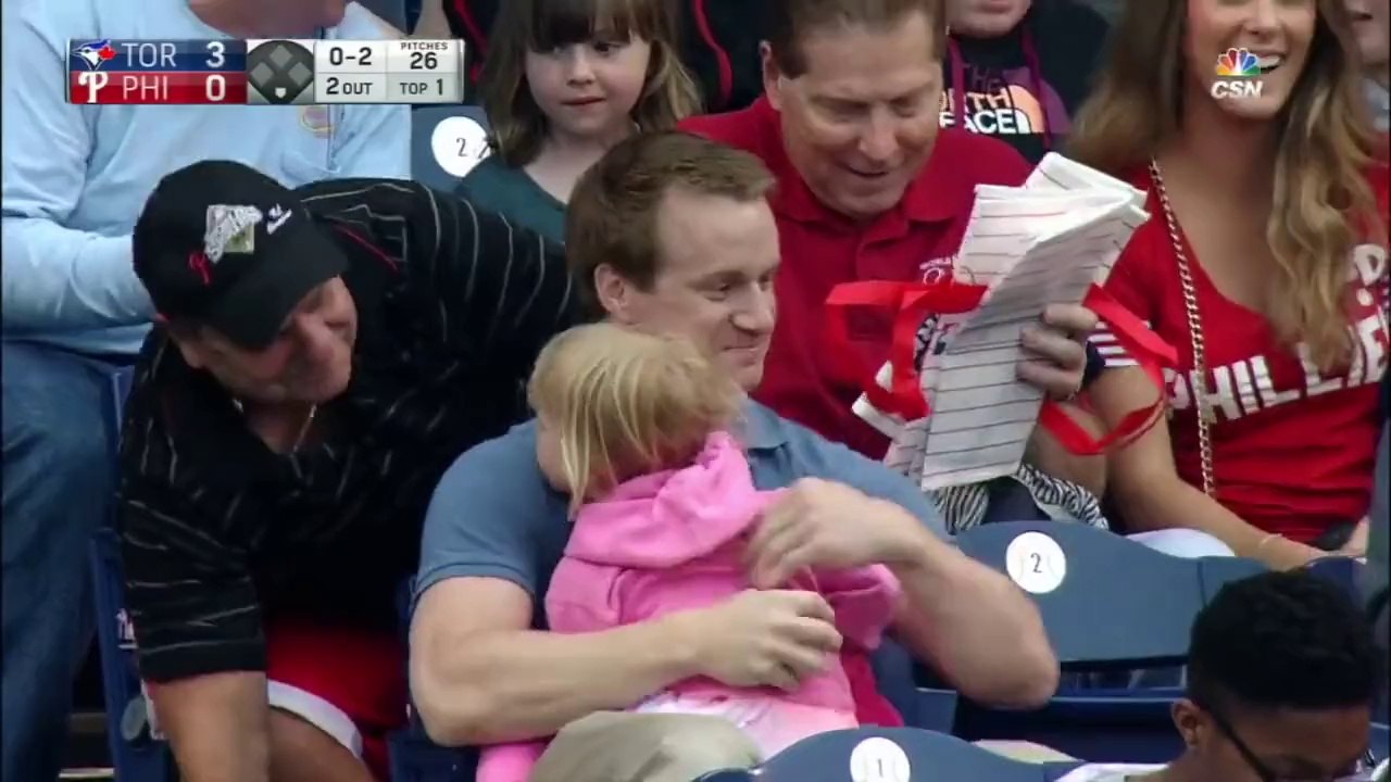 Ce spectateur attrape une balle de baseball tout en tenant sa fille et de la nourriture dans les bras