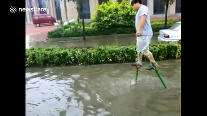 Man walks on stilts to cross flooded road