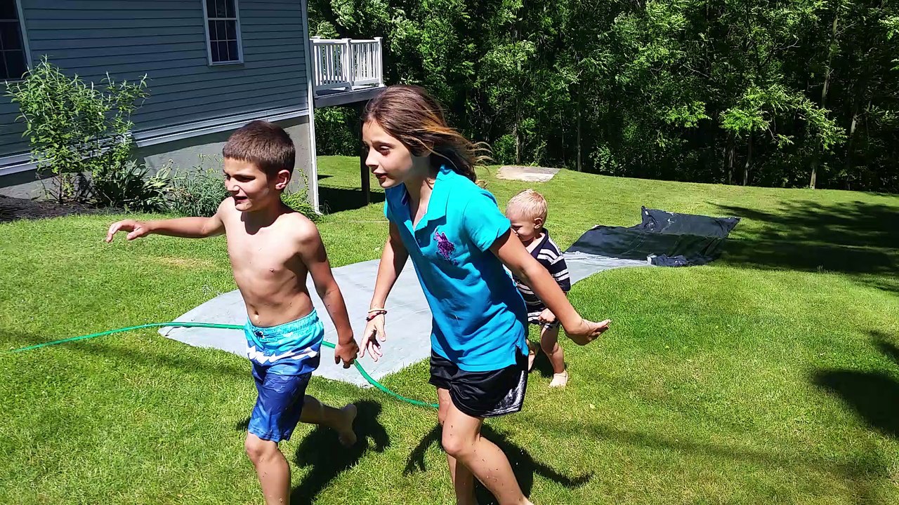 Kids Having Fun On Water Slide Home Made, Down Steep Hill With Mom and Dad Watching