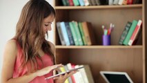 cheerful girl standing beside bookcase using touchpad looking at camera and 4ycnuqhsx  D