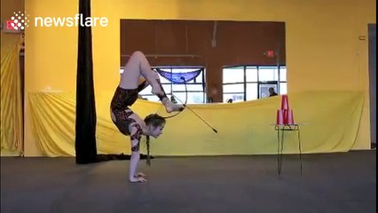 Contortionist fires bow-and-arrow while doing a handstand