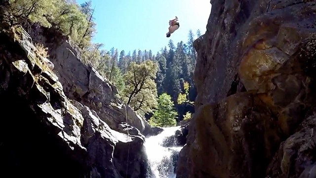 Adventurous Cliff Divers Backflip Beside Picturesque Waterfall
