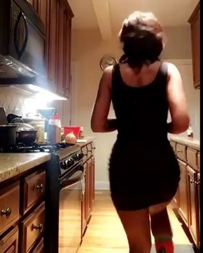 Une femme en robe moulante danse sensuellement dans sa cuisine et glisse