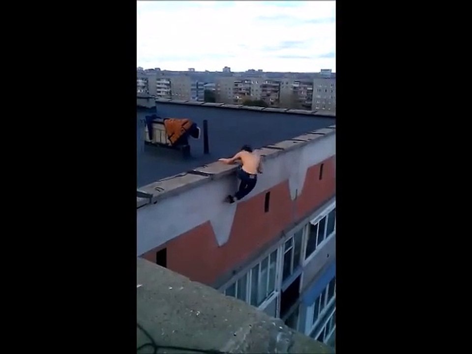 Le gars se suspend dans le vide au sommet d'un immeuble et fait des tractions