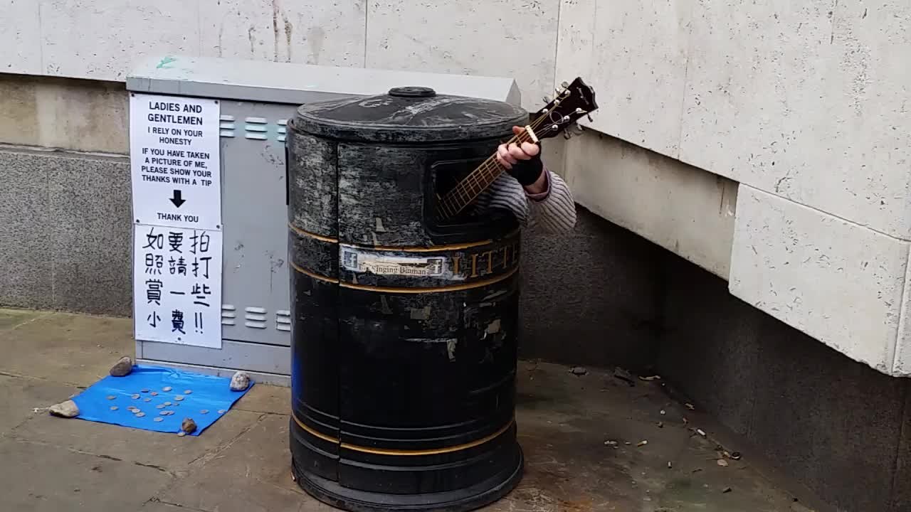 Street performer plays guitar from inside trash bin