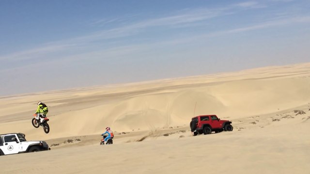 Une motocross fait un saut de 30m dans les dunes et atterrit sur une Jeep