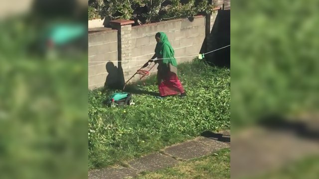 Une femme tente de passer la tondeuse dans son jardin