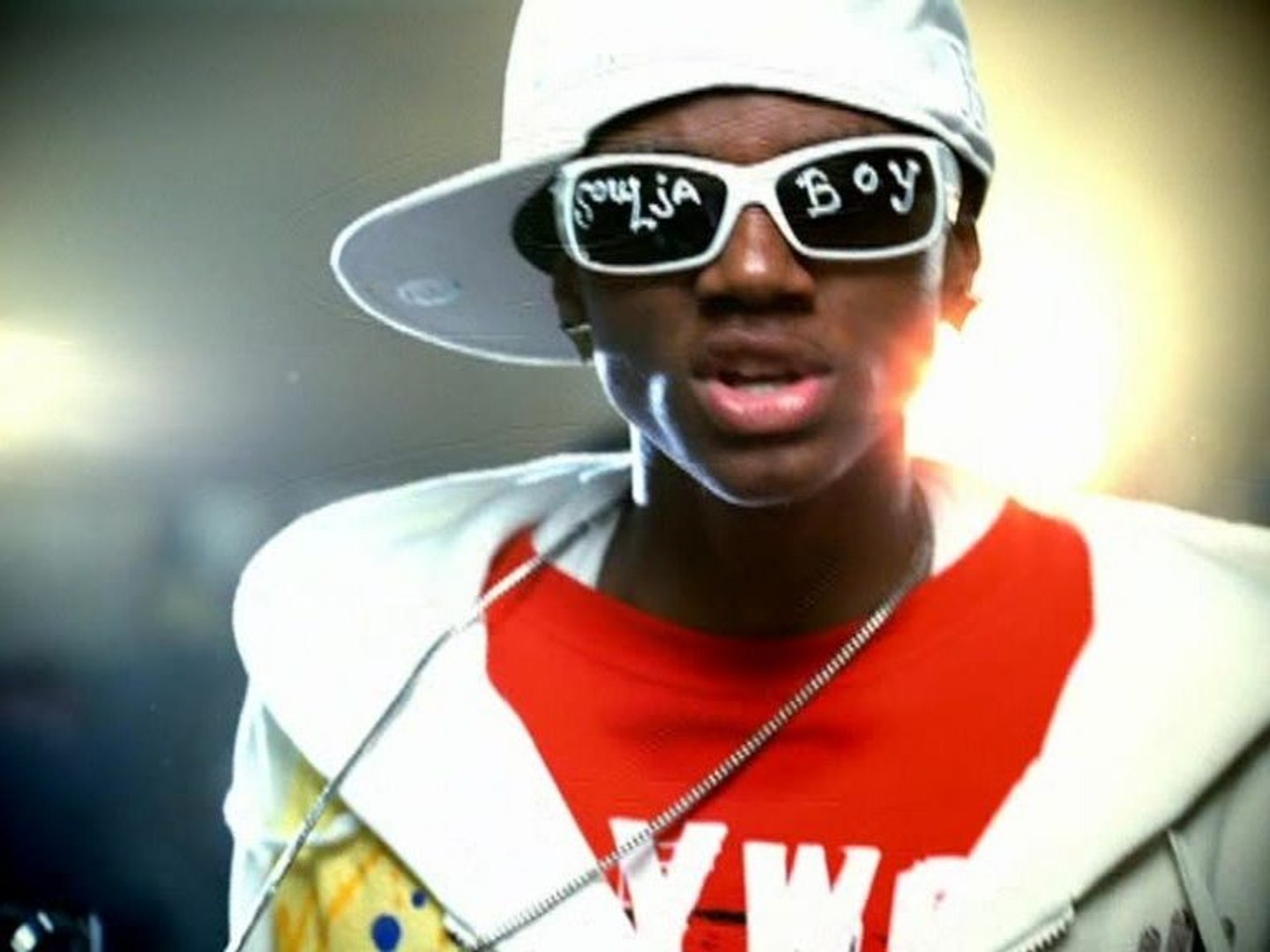Lil Wayne. A young man with shoulder length curly dark hair is captured in a slightly low angle 3 quarter profile view facing left. He is wearing a plain white ribbed tank top that is loose at the sides exposing his torso. He holds a white towel in his hands near his chest. His gaze is directed off to the left.