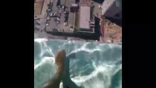 Cet homme marche sur une piscine sur le toit d'un building qui a un fond en verre