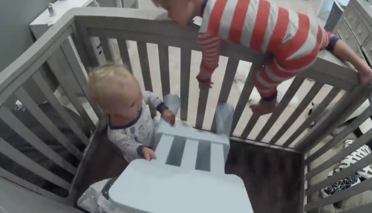 Un petit garçon aide son frère d'un an à s'échapper de son lit à barreaux