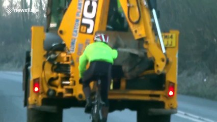 Cyclist holds onto excavator to get uphill