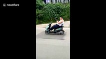 Man drives scooter without holding handle bars while playing on his phone