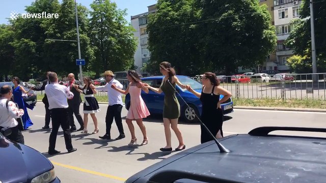 Bulgarian wedding-goers dance on a busy road