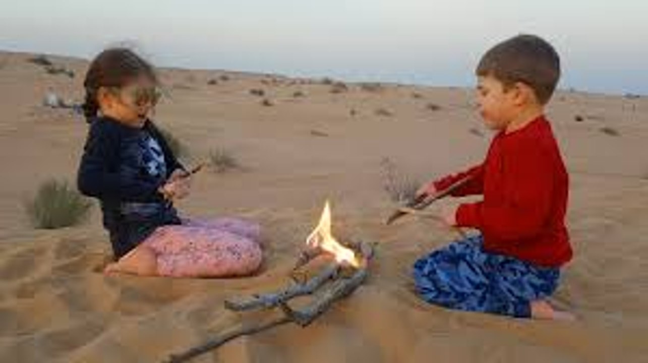 Kids playing with sand in the desert. They pretend  have slides, and do fire