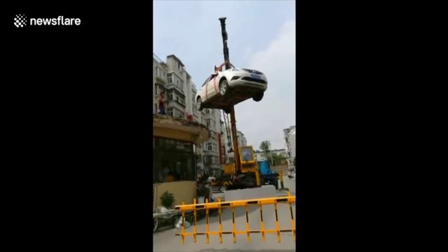 Une grue porte cette voiture mal garée sur le toît de la cabine du Parking !