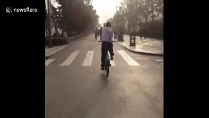 Chinese man does Tai Chi while riding bike on busy road