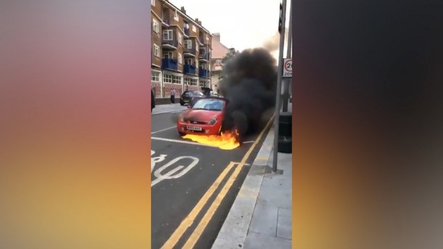 Bystanders attempt to stop a burning car rolling along a busy London street