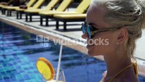 sensual-blond-woman-wearing-crochet-bikini-and-sunglasses-smiling-drinking-orange-juice-and-enjoying-summer-day-while
