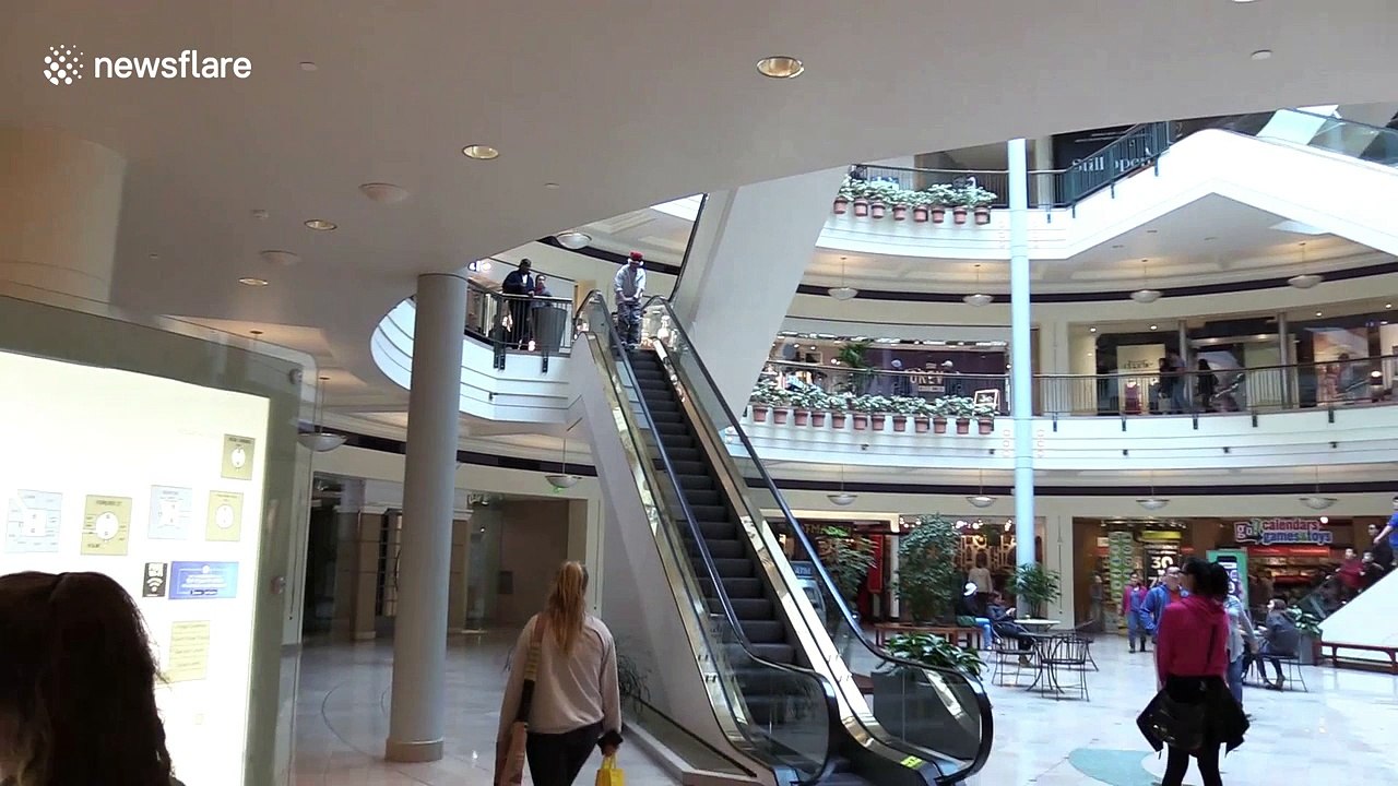 Man in Santa Claus hat descends shopping mall escalator on skis
