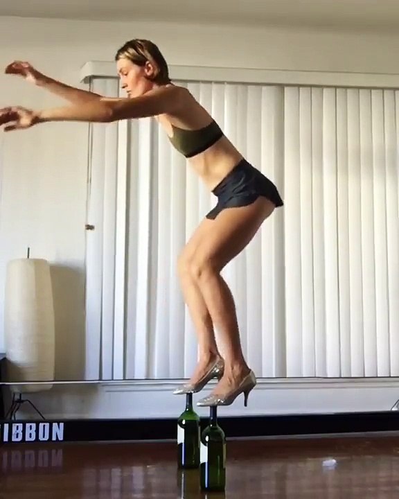 En talons elle fait des squatts sur des bouteilles de vin en équilibre !