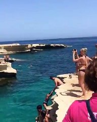 Un petit chien saute dans l'eau d'une falaise en même temps que son maître