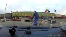 De locos  ciclista pasa entre dos trenes en un paso a nivel