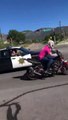 Un policier braque son arme sur un motard qui fait un wheeling.