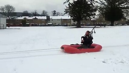 Jouer de la cornemuse tracté dans la neige par un quad