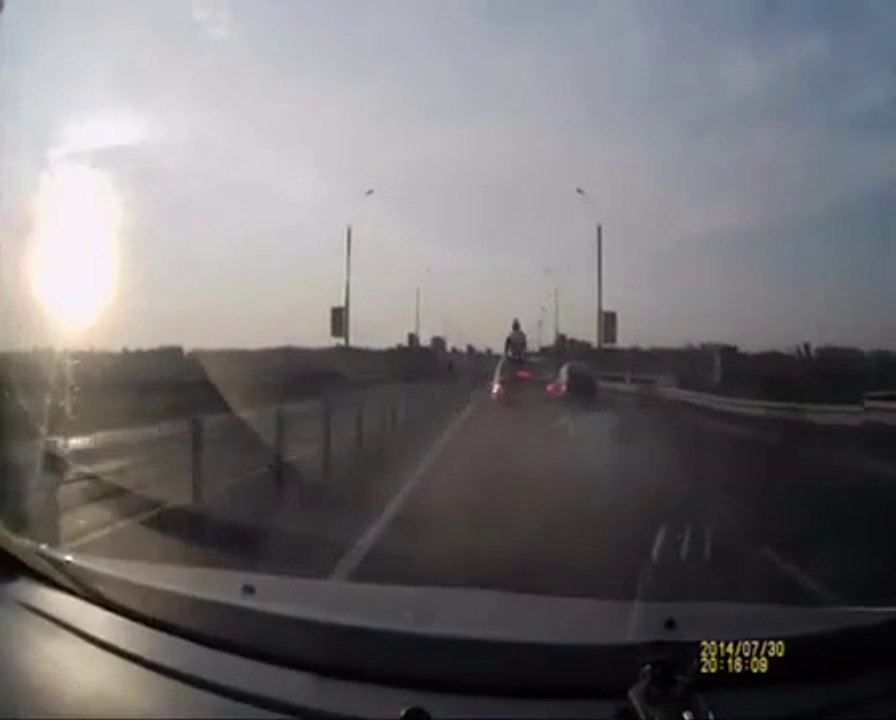 Un motard chanceux se retrouve debout sur le toit d'une voiture